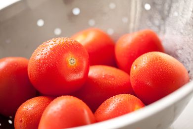 Macro of Fresh, Vibrant Roma Tomatoes in Colander with Water Drops Abstract.