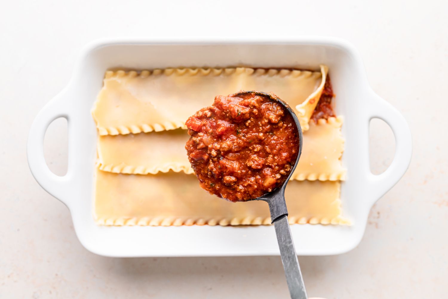 Spreading sauce over noodles in a pan to show how to make lasagna.