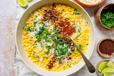 Bowl of Esquites Topped with Cilantro, Cotija Cheese, and Ancho Chile Pepper Surrounded by Bowls of Toppings