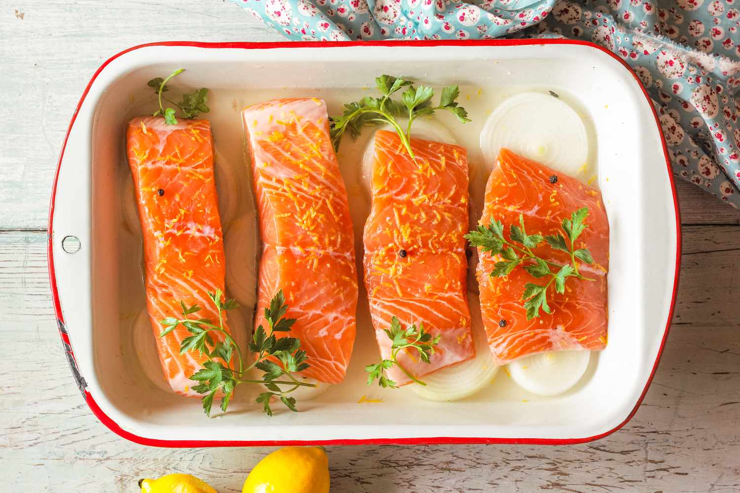 Overhead view of four raw salmon fillets in a baking dish