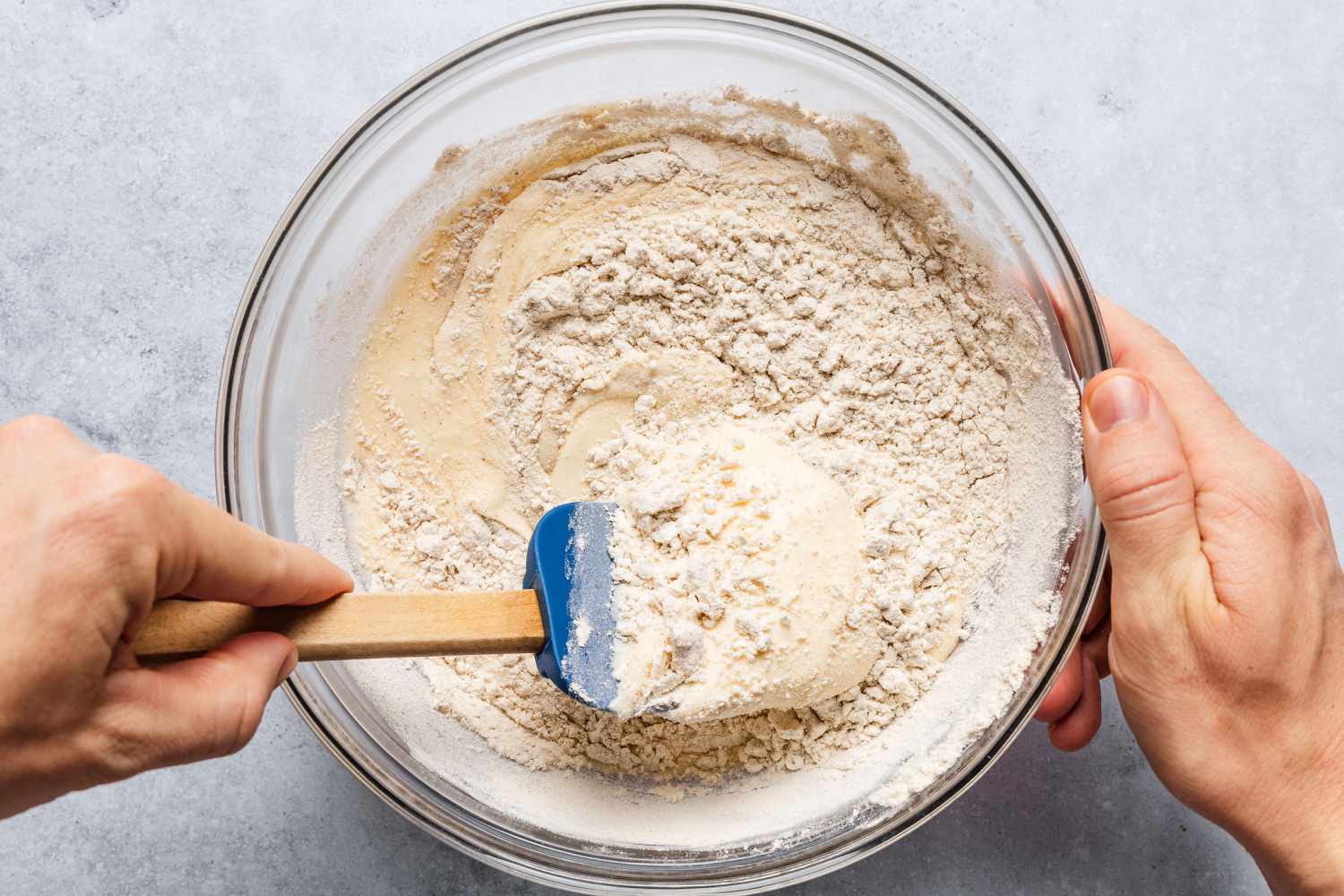 hand with rubber spatula stirring dry ingredients into wet ingredients in a bowl - Feather Cake