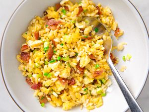Bowl of fried rice with egg, bacon, and green onions, spoon included