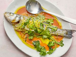 Overhead view of a steamed whole fish on a flatter and topped with sauce and herbs.