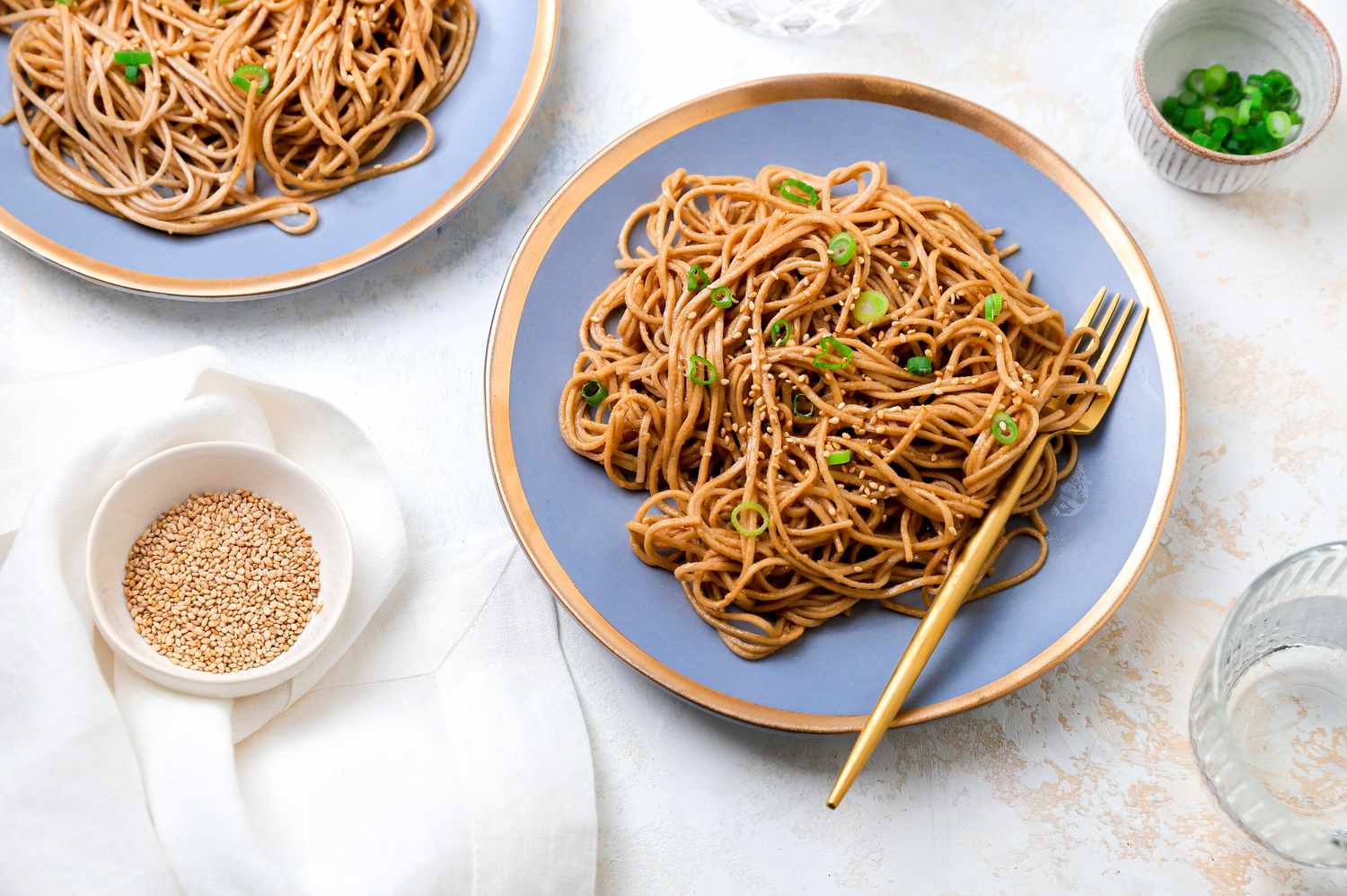 Plates of Sesame Peanut Noodles Next to a Small Bowls of Sesame Seeds and Green Onions