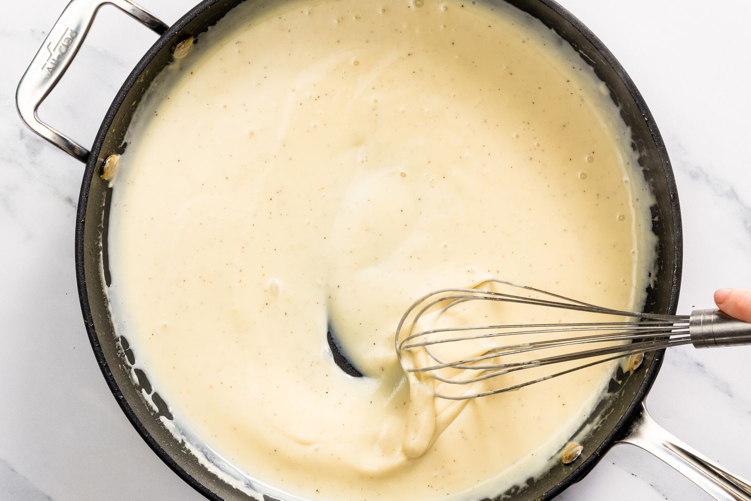 sauce thickening in pan with hand whisking it for Church Chicken Casserole