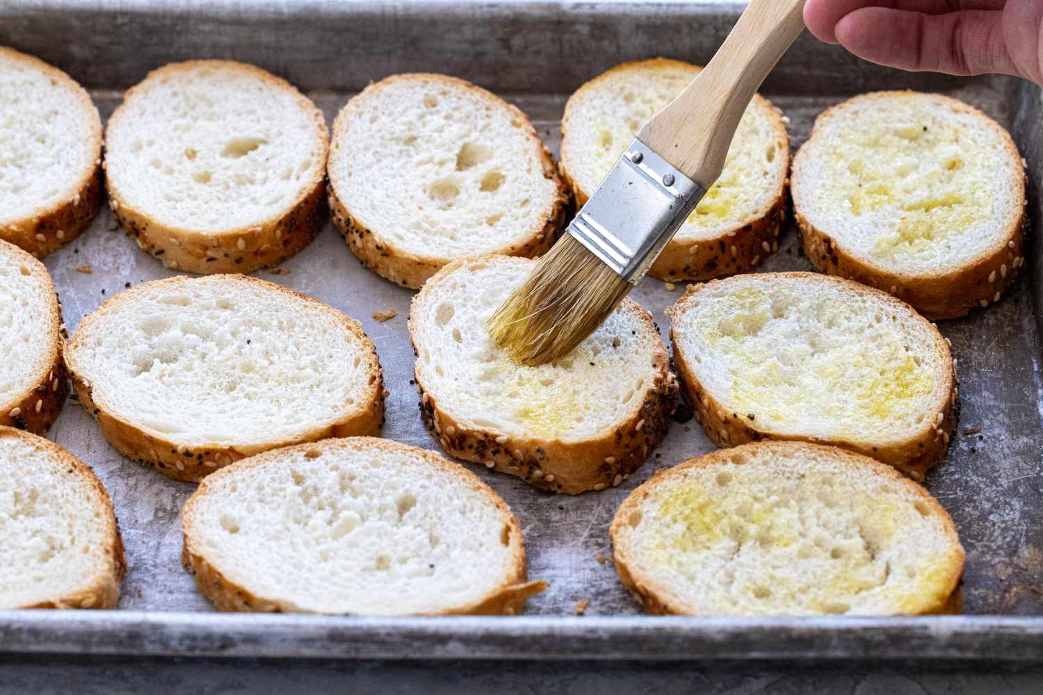 Brushing crostinis with oil on a baking sheet to make smoked salmon crostinis.