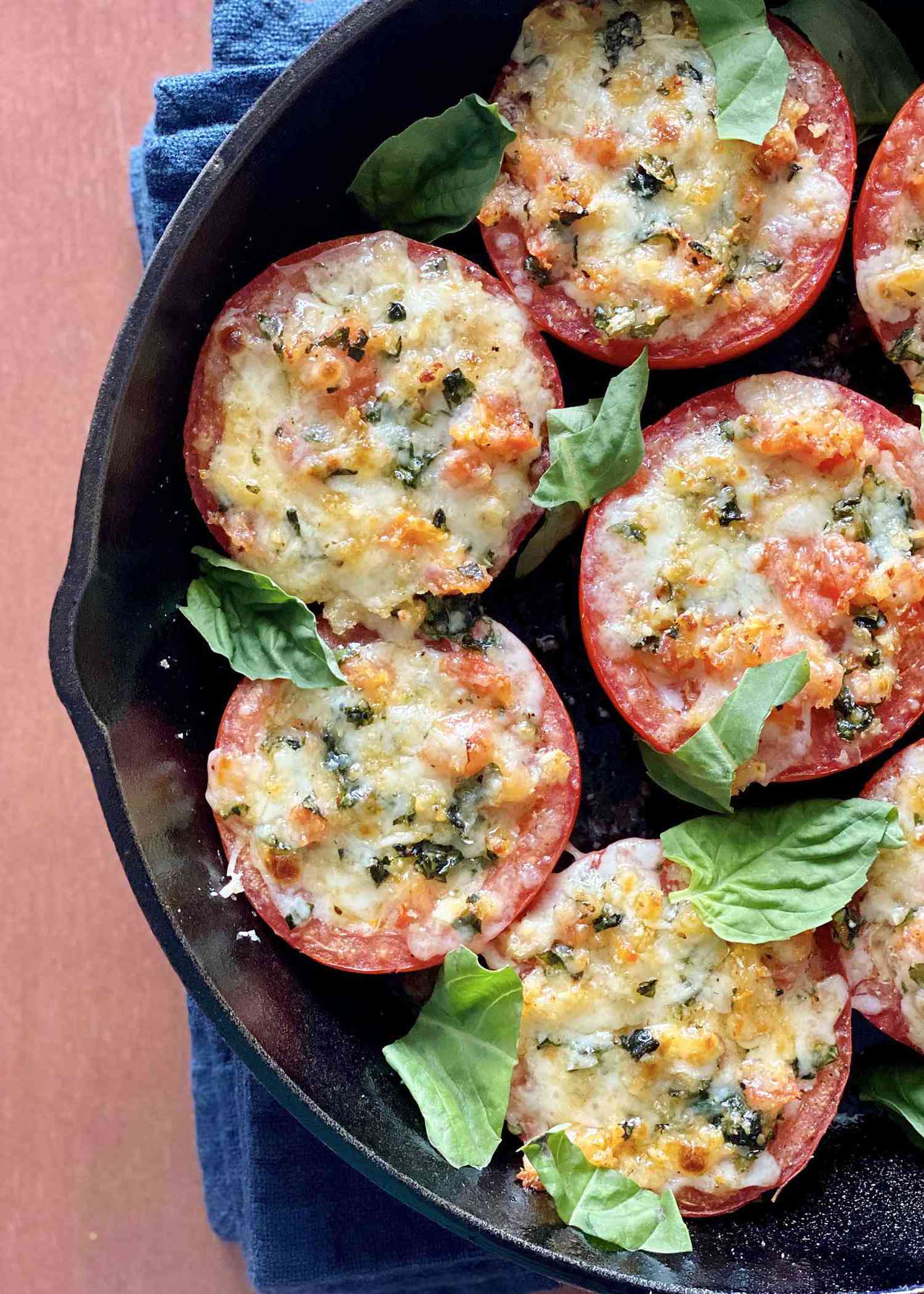 Overhead view of a cast iron skillet with vegetarian stuffed tomatoes with basil leaves scattered over top.