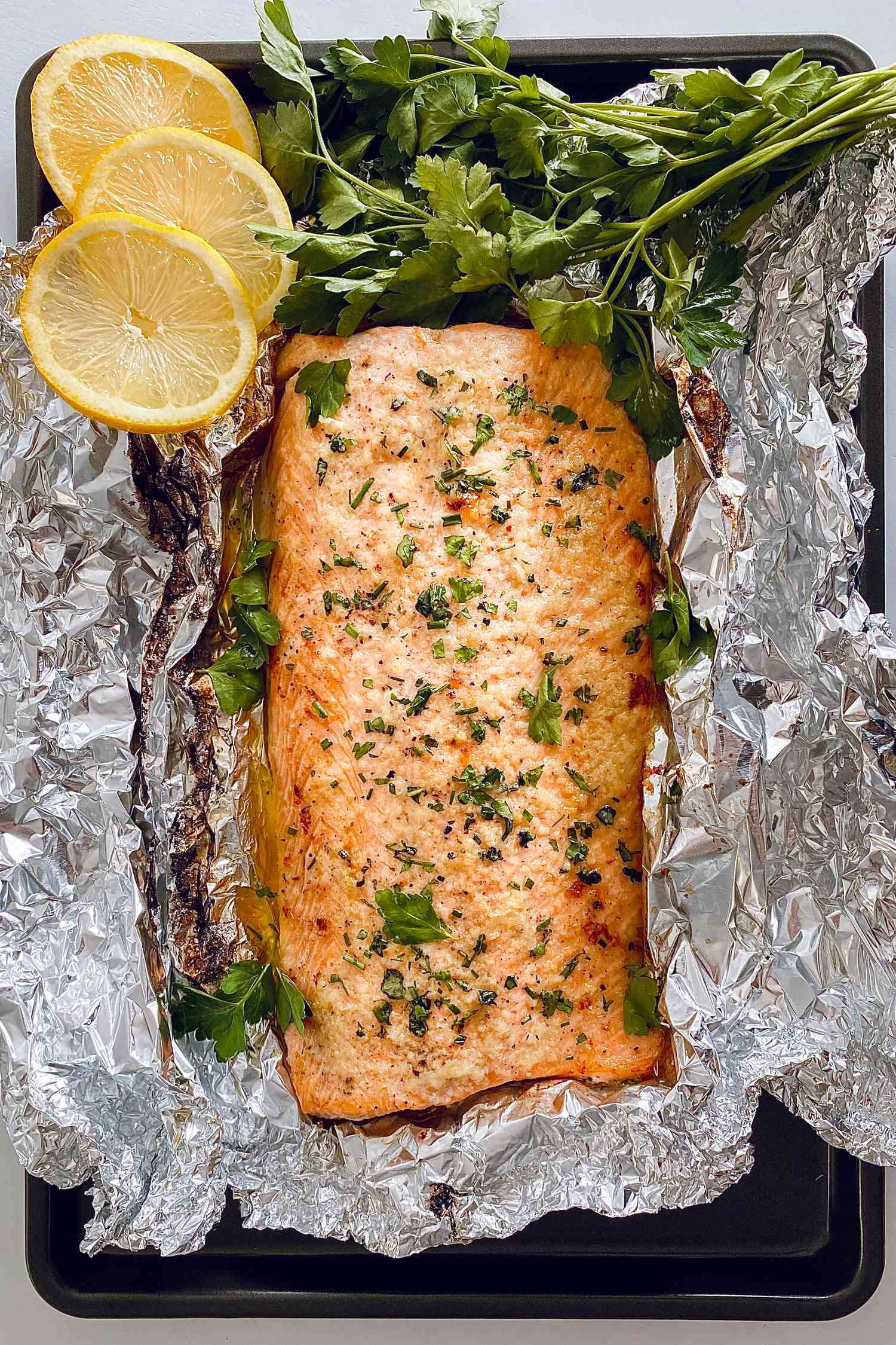 Overhead of a garlic butter roasted salmon on foil with herbs and lemon