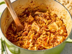 Onepot ground beef and cabbage dish being cooked in a green Dutch oven with a wooden spoon