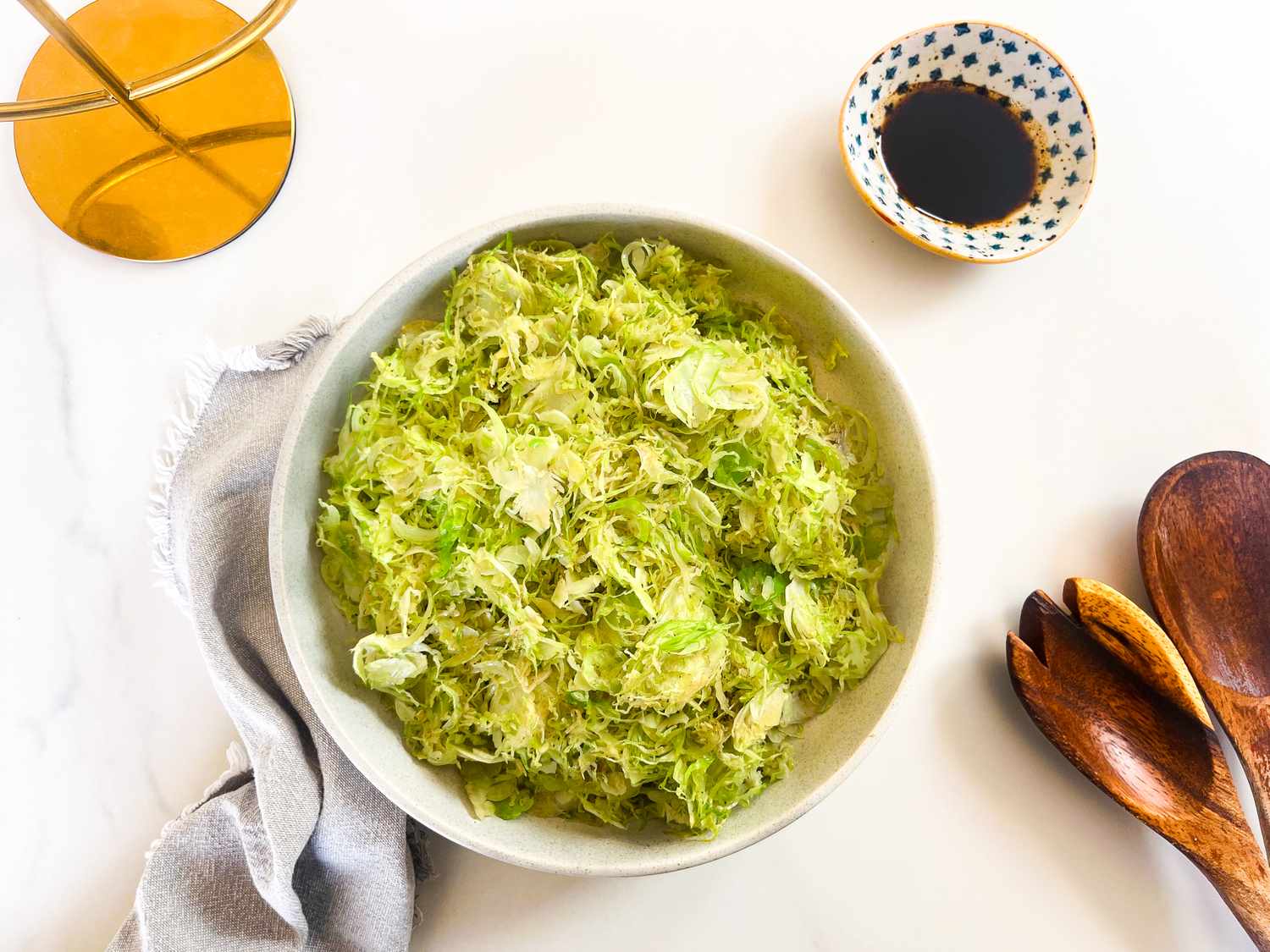 Shredded Brussels sprouts in a bowl small dish with dark sauce wooden utensils next to the bowl