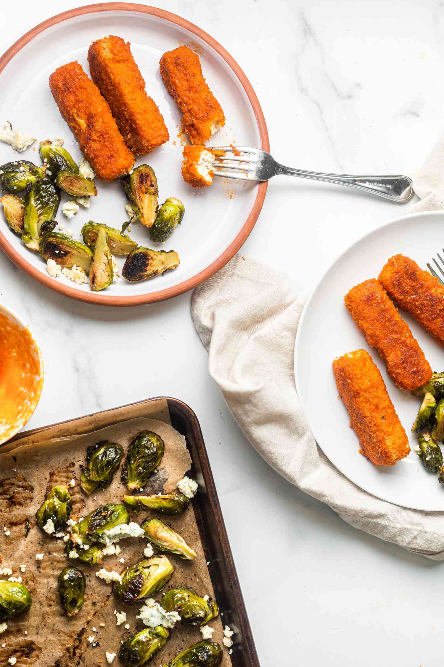 Sheet Pan Buffalo Tofu and Blue Cheese Brussels Sprouts on Two Plates Next to a Baking Tray with More Brussel Sprouts