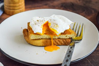 Side view of a poached egg on halved toast with the yolk running over the side.