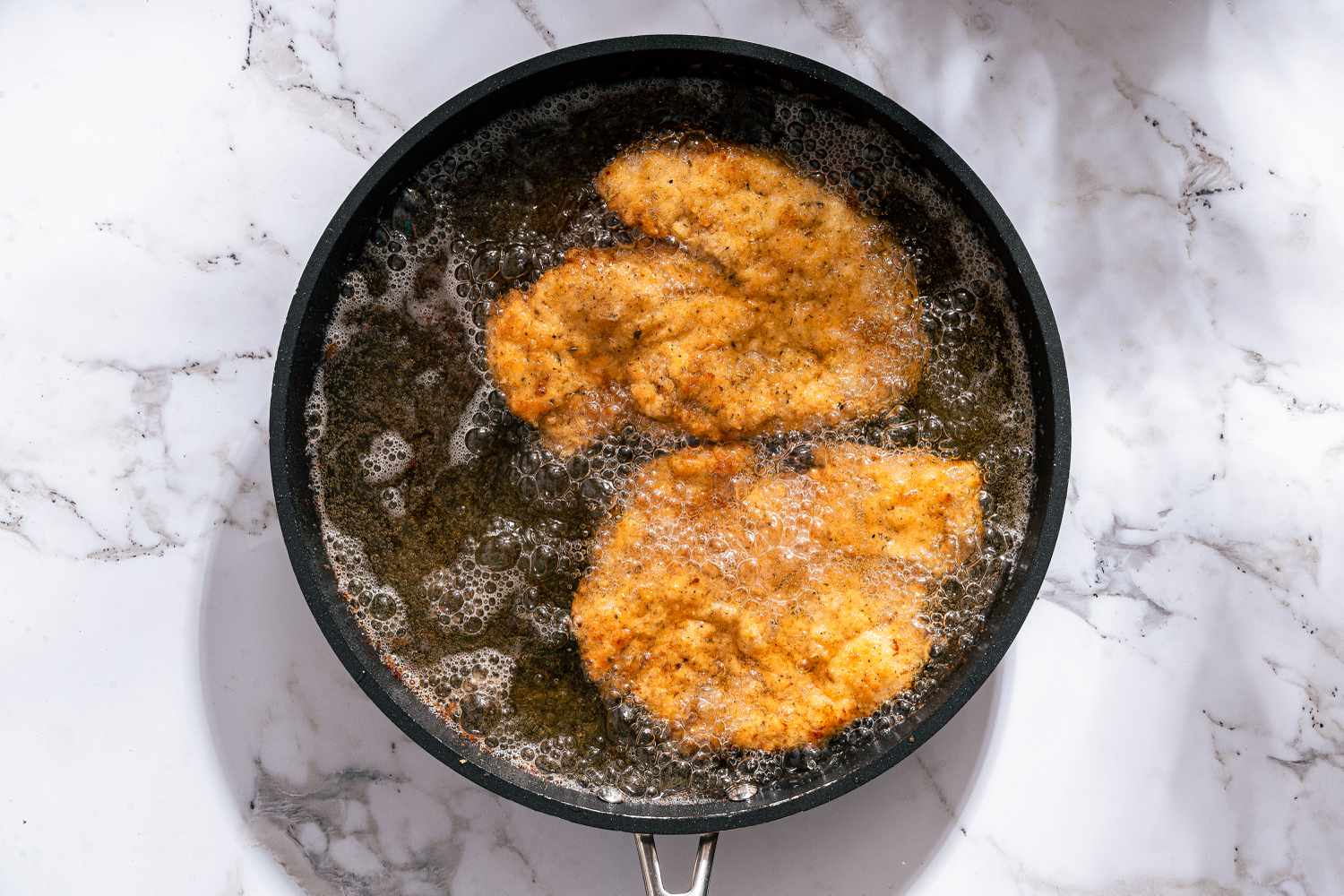 two chicken cutlets being pan fried until golden brown for Chicken Romano