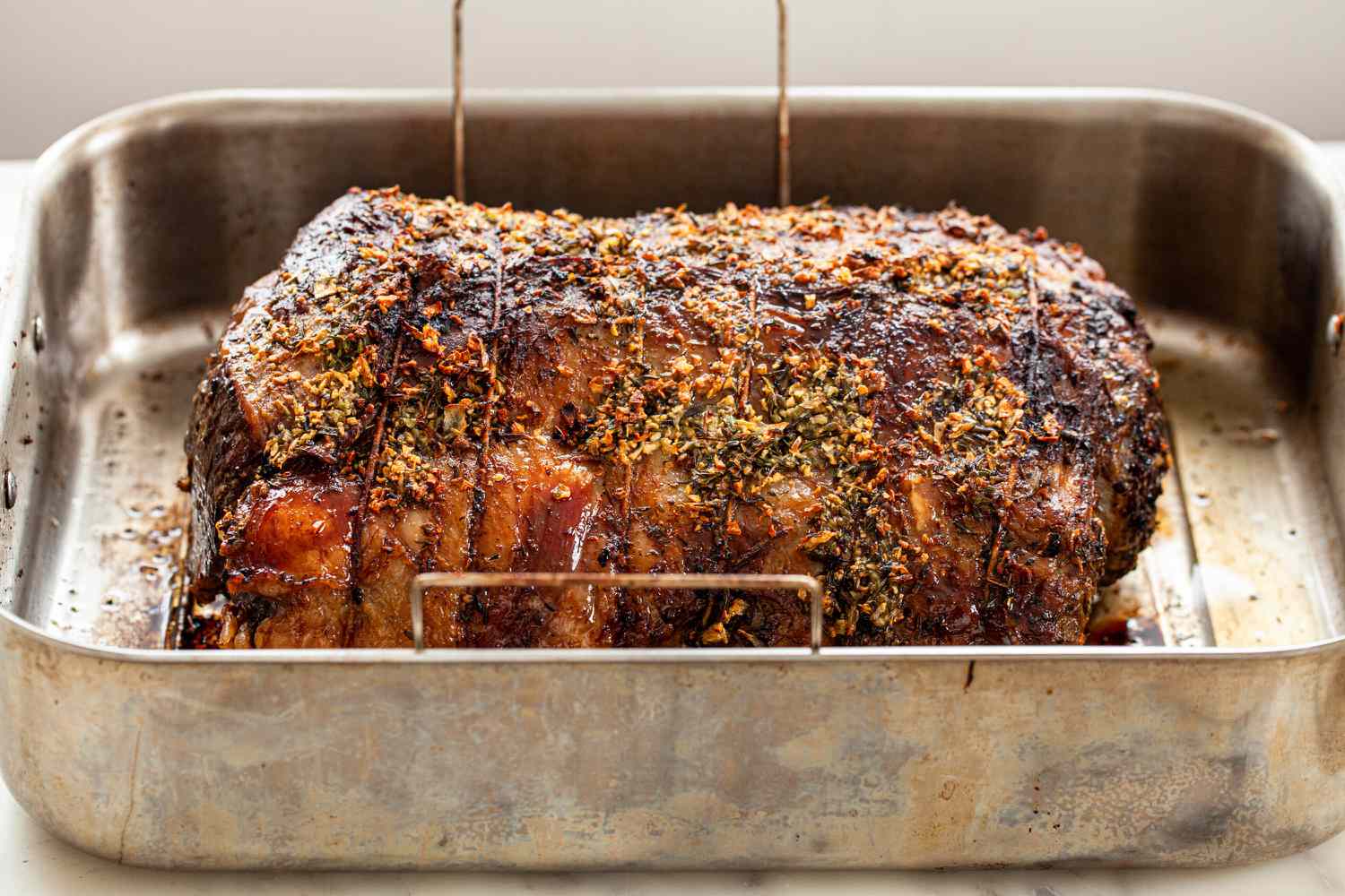 Herb butter prime rib with gravy resting in a roasting pan.