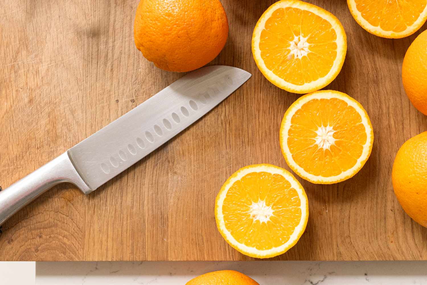 A knife on a wooden cutting board surrounded by orange slices