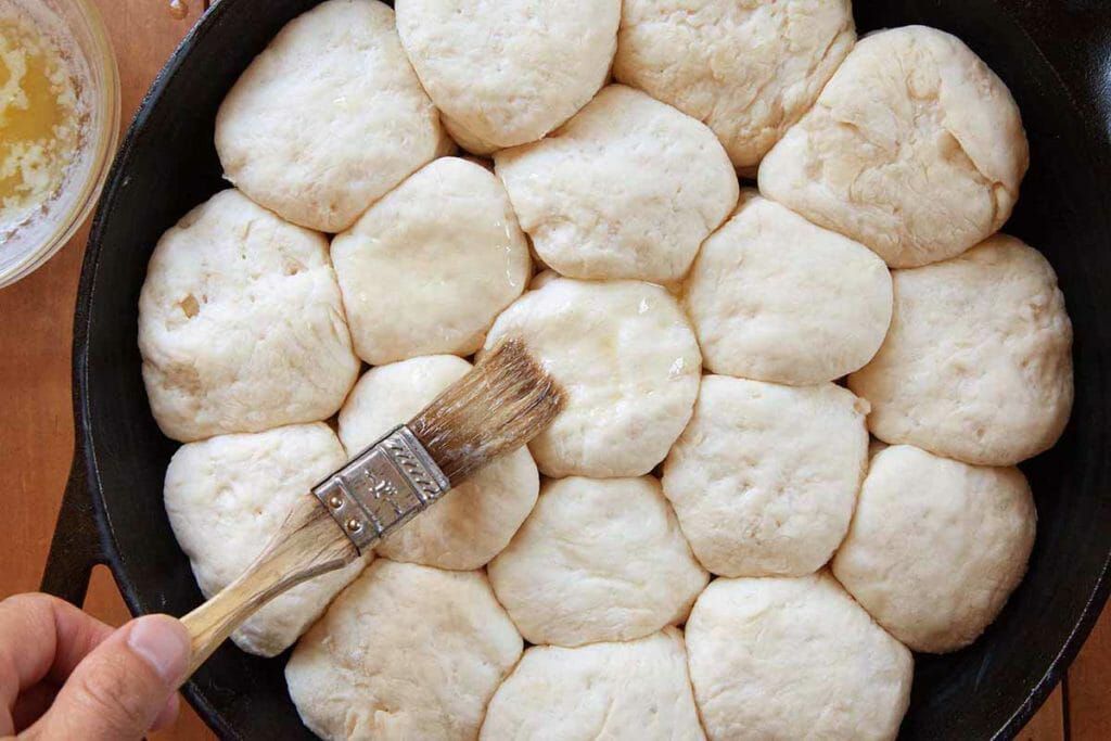 Brush angel biscuit dough with butter before baking in a cast iron skillet