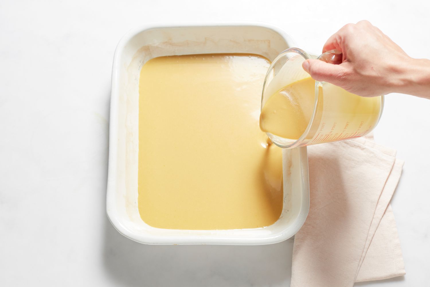 Pouring batter and spreading bean paste on a Sticky rice cake with red bean paste in a baking dish.