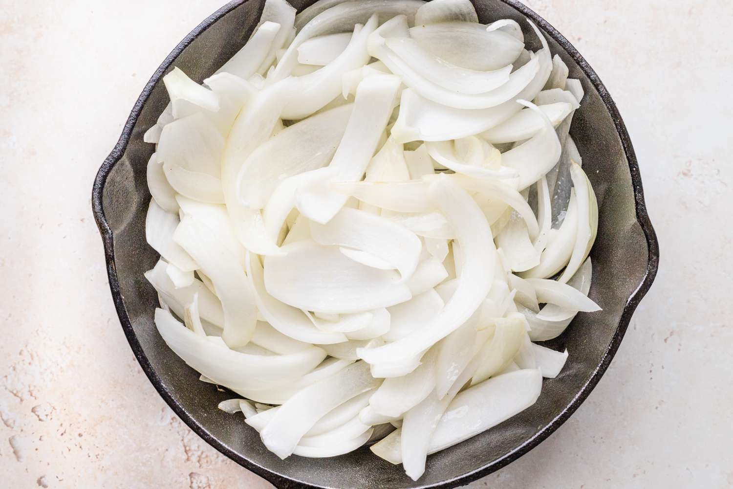 Overhead of sliced onions in a cast iron skillet resting on a counter top