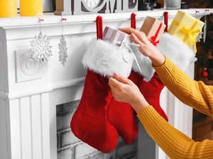A person placing gifts into red stockings hanging from a mantel