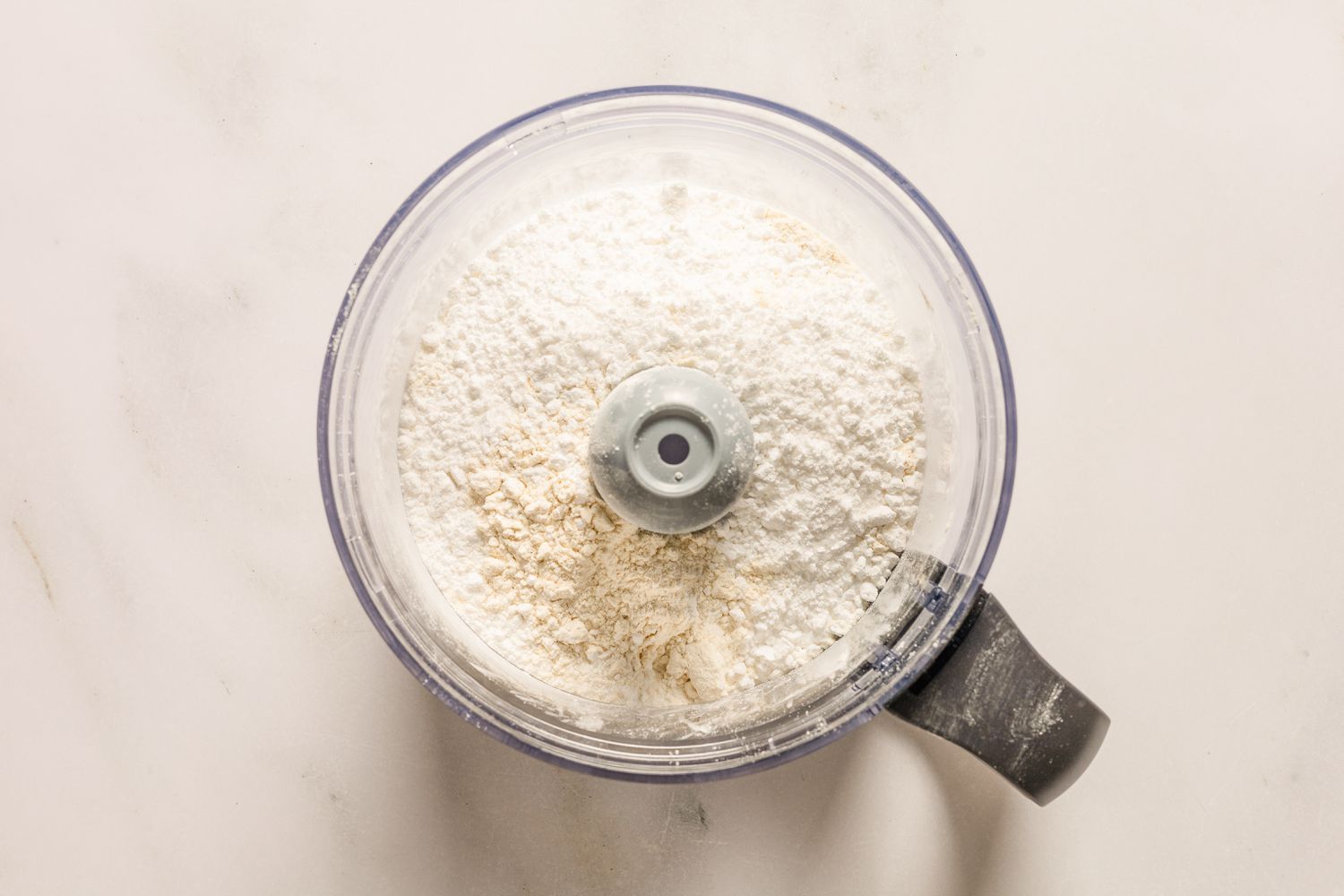 An overhead view of a food processor bowl with the dry ingredients for Sand Tarts recipe