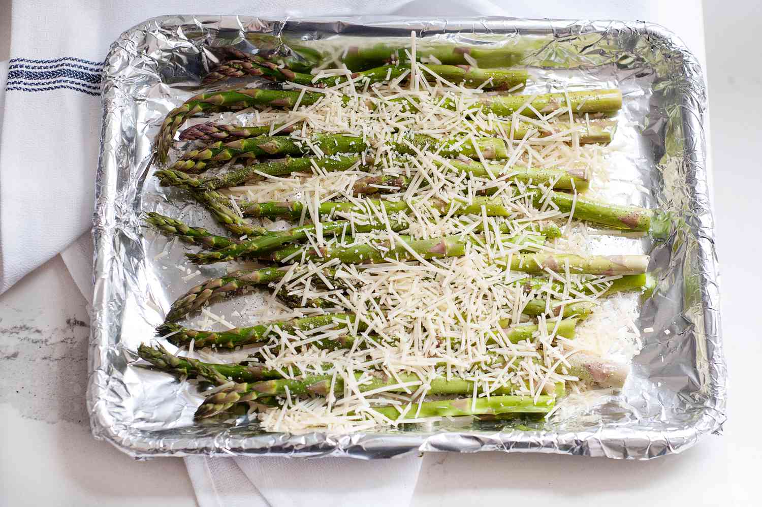 A baking tray with asparagus topped with parmesan to show how to cook asparagus in the oven.