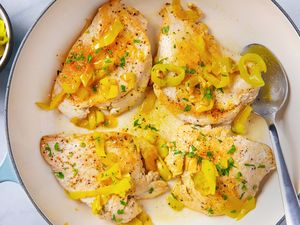 A skillet with cooked chicken breasts topped with banana peppers and garnished with herbs