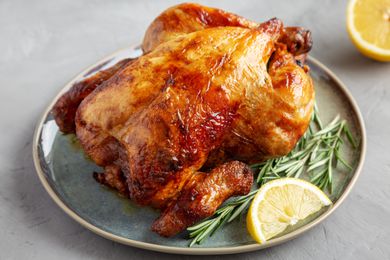 A crispy skinned roasted chicken on a plate, with rosemary sprigs and a lemon wedge as garnish