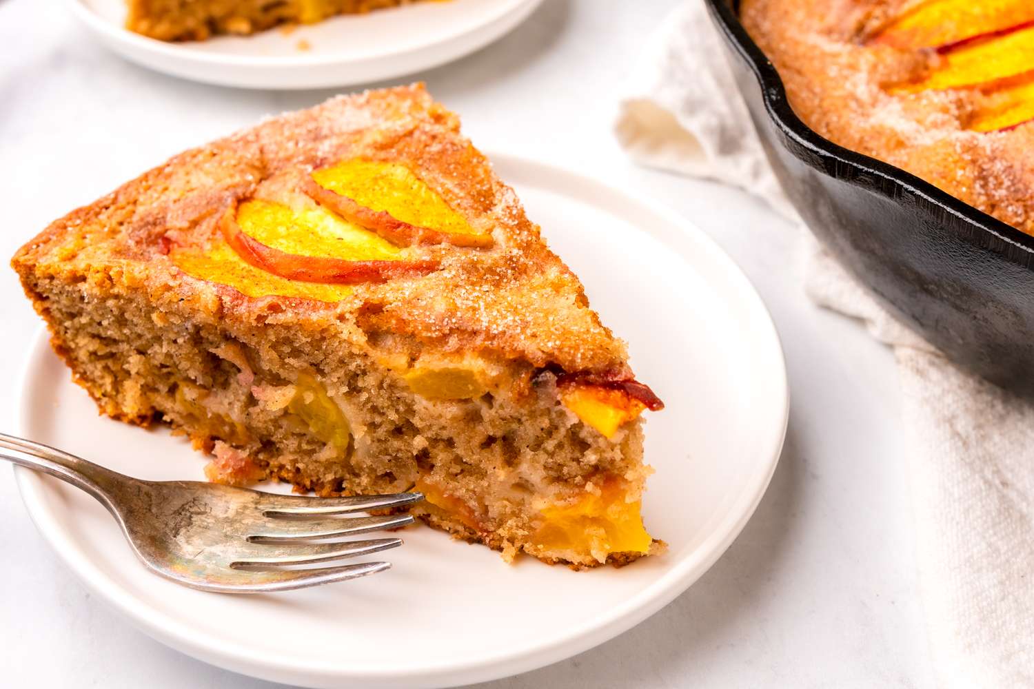 A slice of skillet peach cake on a white plate with a fork