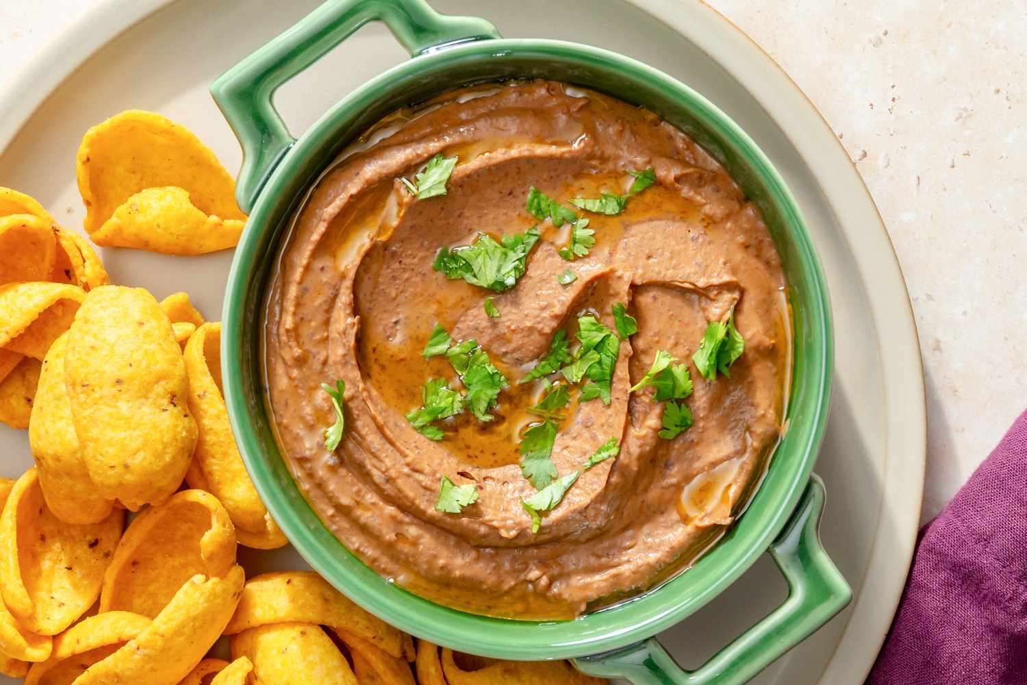 Bowl of black bean dip garnished with herbs surrounded by corn chips on a plate