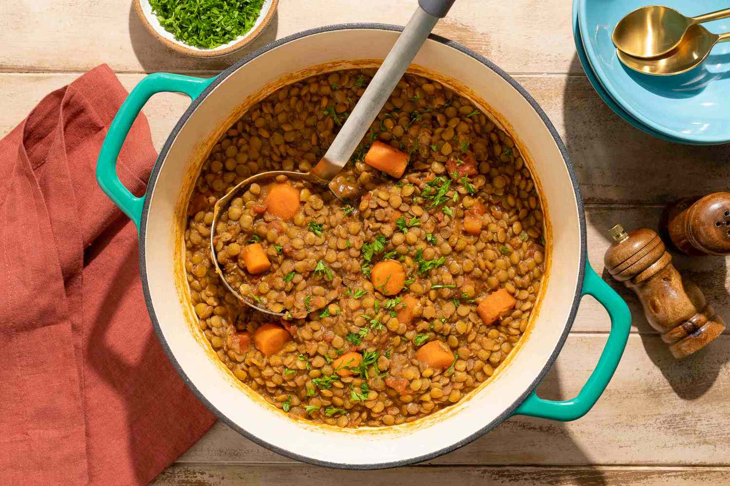 A pot of cooked spiced lentils with diced vegetables and a ladle garnished with fresh herbs on top