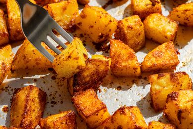 Cubed roasted potatoes with dark-spiced char, a fork lifting one piece