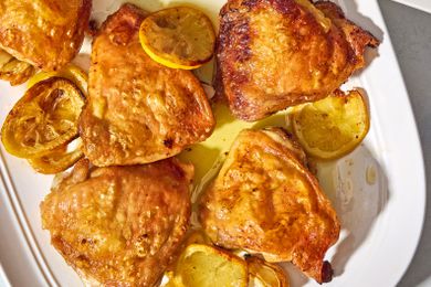 Overhead closeup view of a white serving platter of lemon chicken thighs and lemon slices