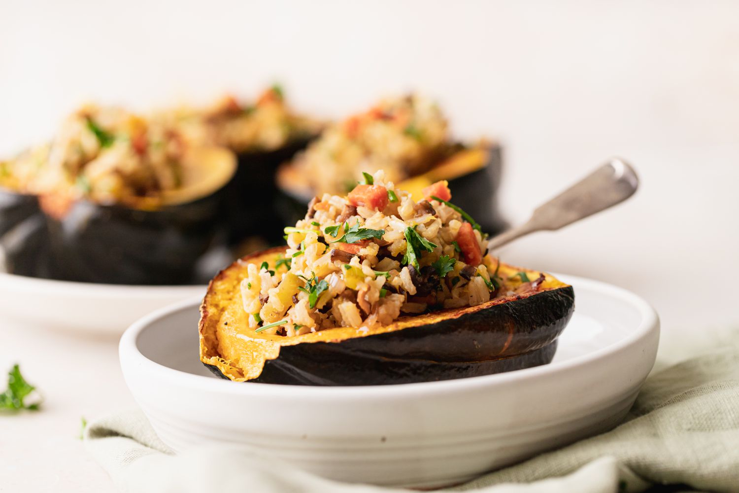 Side view of a vegan acorn squash in a low bowl and additional squash set behind it.