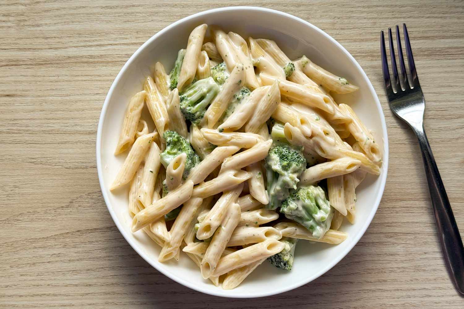 A bowl of creamy macaroni and cheese with broccoli on a wooden surface