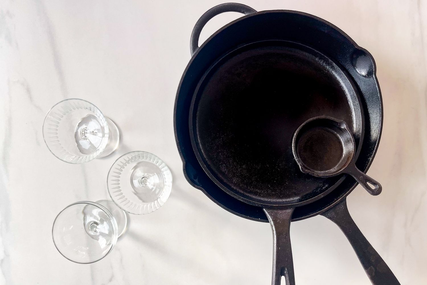 Cast iron pans and glassware arranged on a marble surface