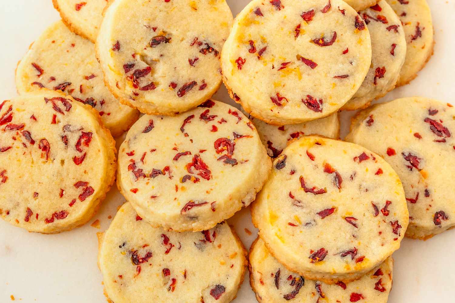Overhead view of multiple cranberry orange shortbread cookies on an off-white background