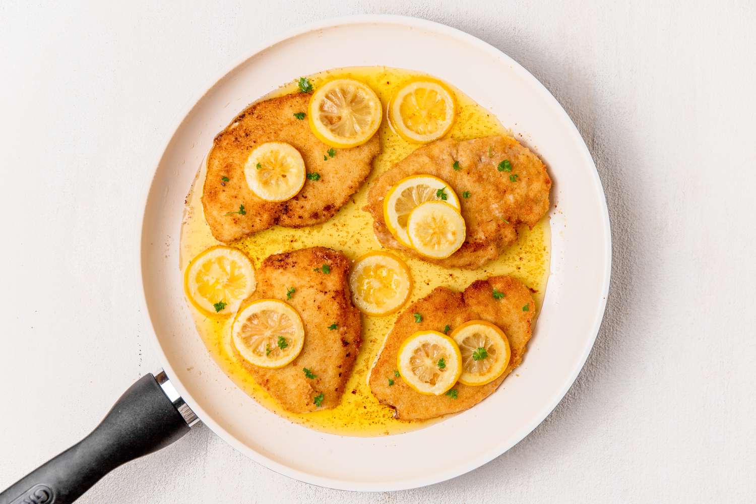 Italian butter chicken (petti di pollo al burro) in a skillet topped with lemon slices and minced parsley