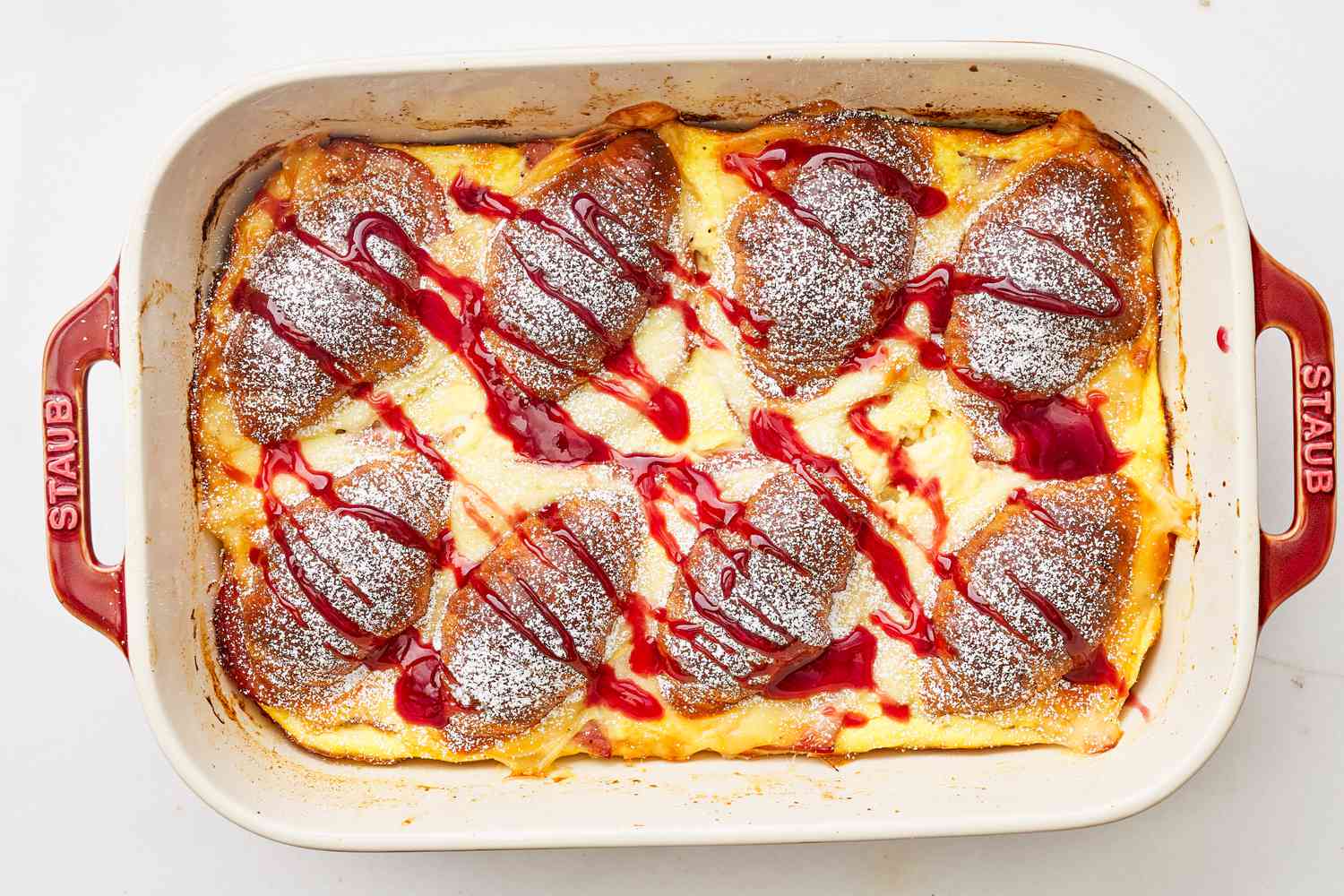 Monte cristo croissant casserole topped with powdered sugar and a jelly drizzle 