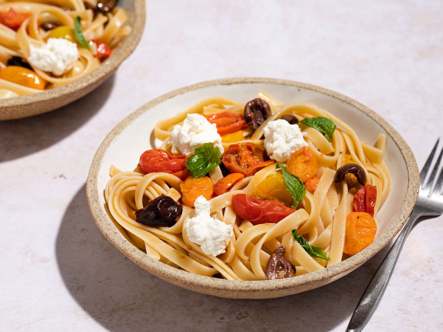 A bowl with Jamie Oliver's 12-minute pasta; fettucine pasta with olives, tomatoes and dollops of ricotta and basil leaves as garnish