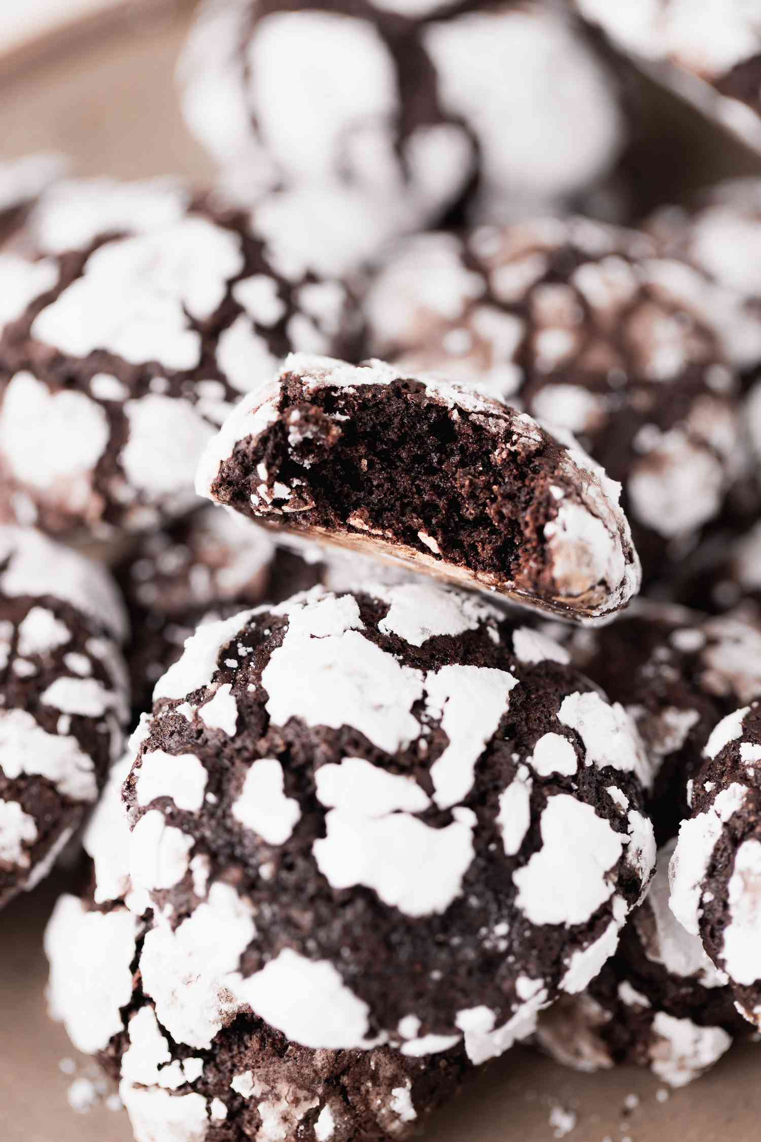 A plate of chocolate crinkle cookies with a bite taken out of the cookie on the top.