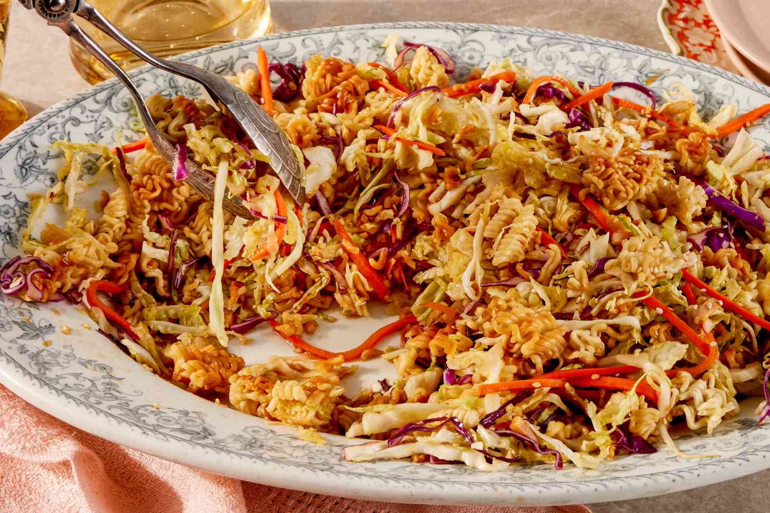 Angled view of a decorative serving platter of crunchy ramen salad with serving scoops