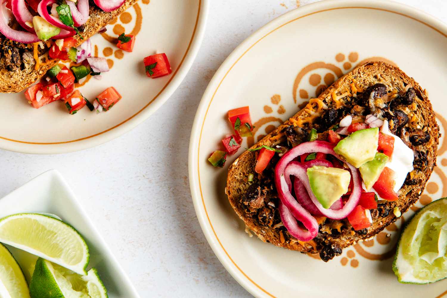 Black bean toast on a plate next to another plate with a serving and a bowl of lime slices