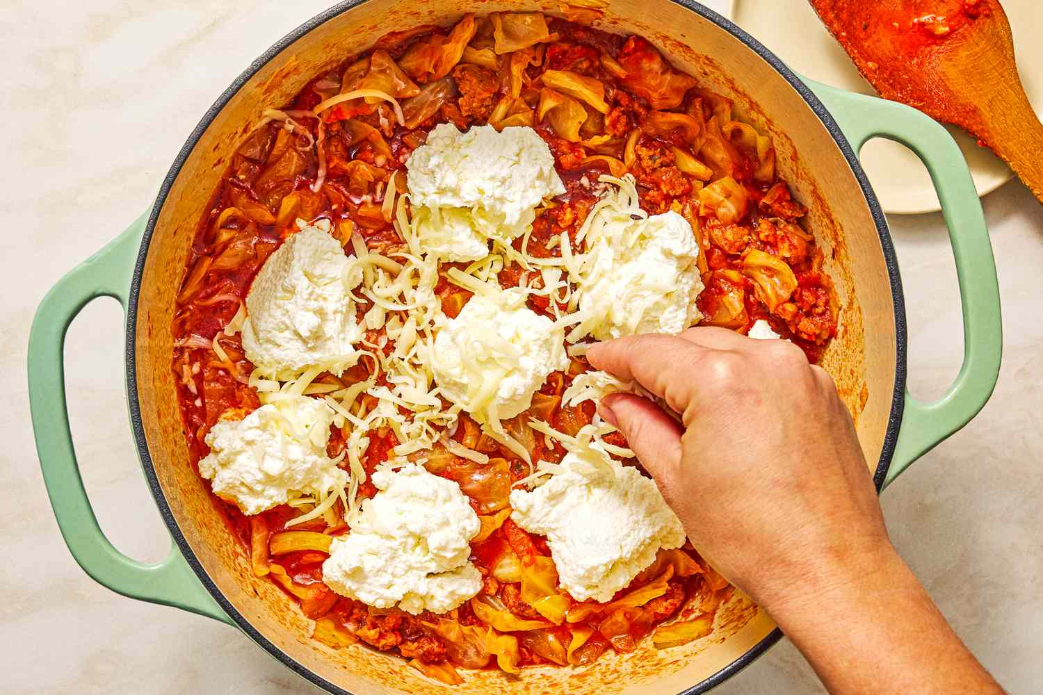 Cabbage lasagna getting cooked in a pot layers with ricotta cheese being added for the 5-Ingredient Braised Cabbage “Lasagna” recipe
