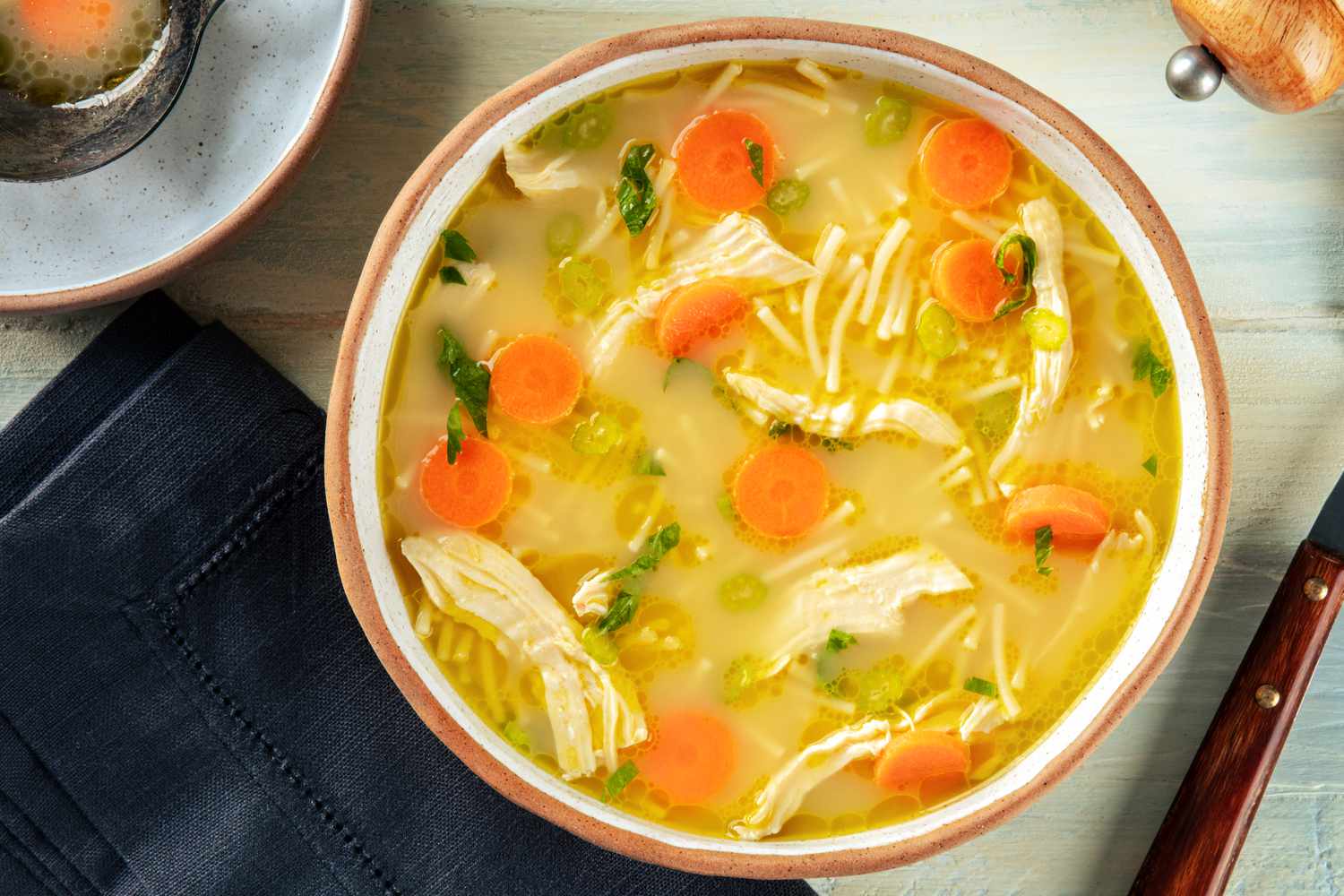 A photo of a bowl of chicken soup with carrot rounds and shredded chicken
