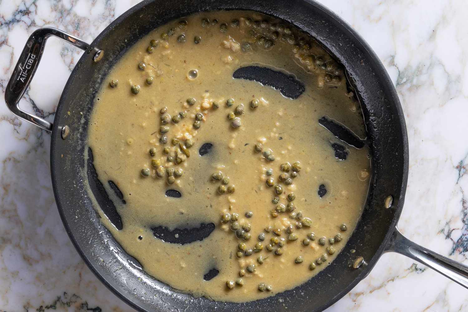 capers added to sauce in pan for Salmon Piccata