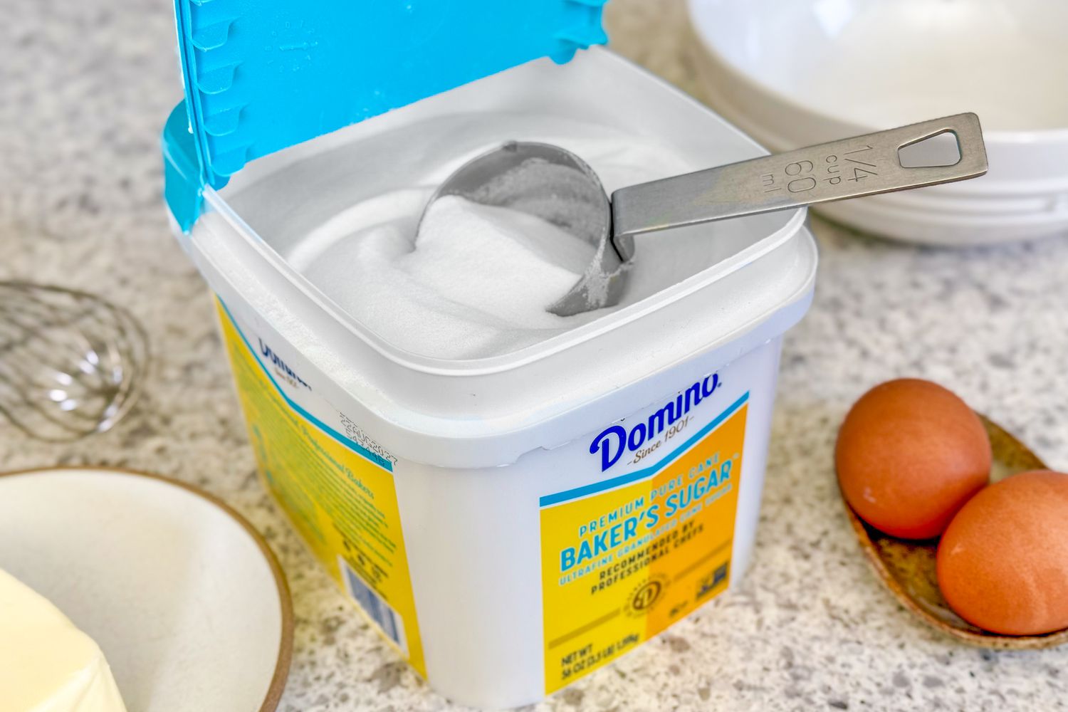 Domino baker's sugar container with a measuring cup, displayed with eggs and ingredients in the background