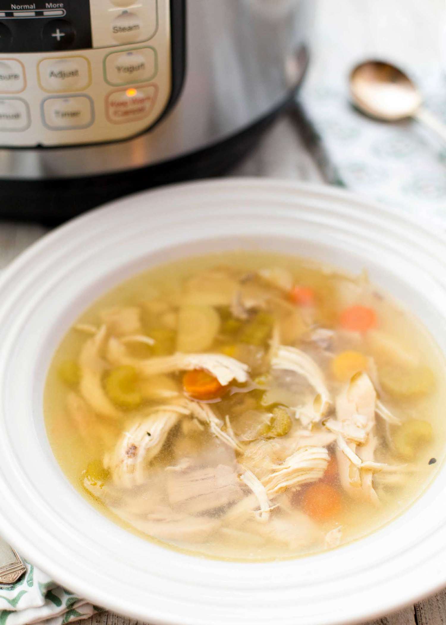 Bowl of chicken soup with vegetables in front of a pressure cooker