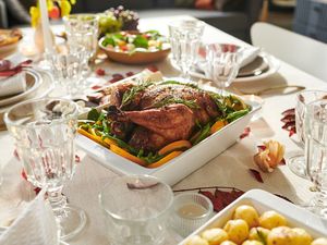 A roasted turkey served at a dinner table set with plates glasses and side dishes for Thanksgiving