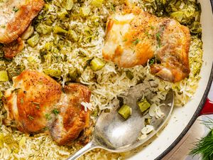 Cooked chicken thighs on a bed of rice with chopped pickles and herbs in a skillet