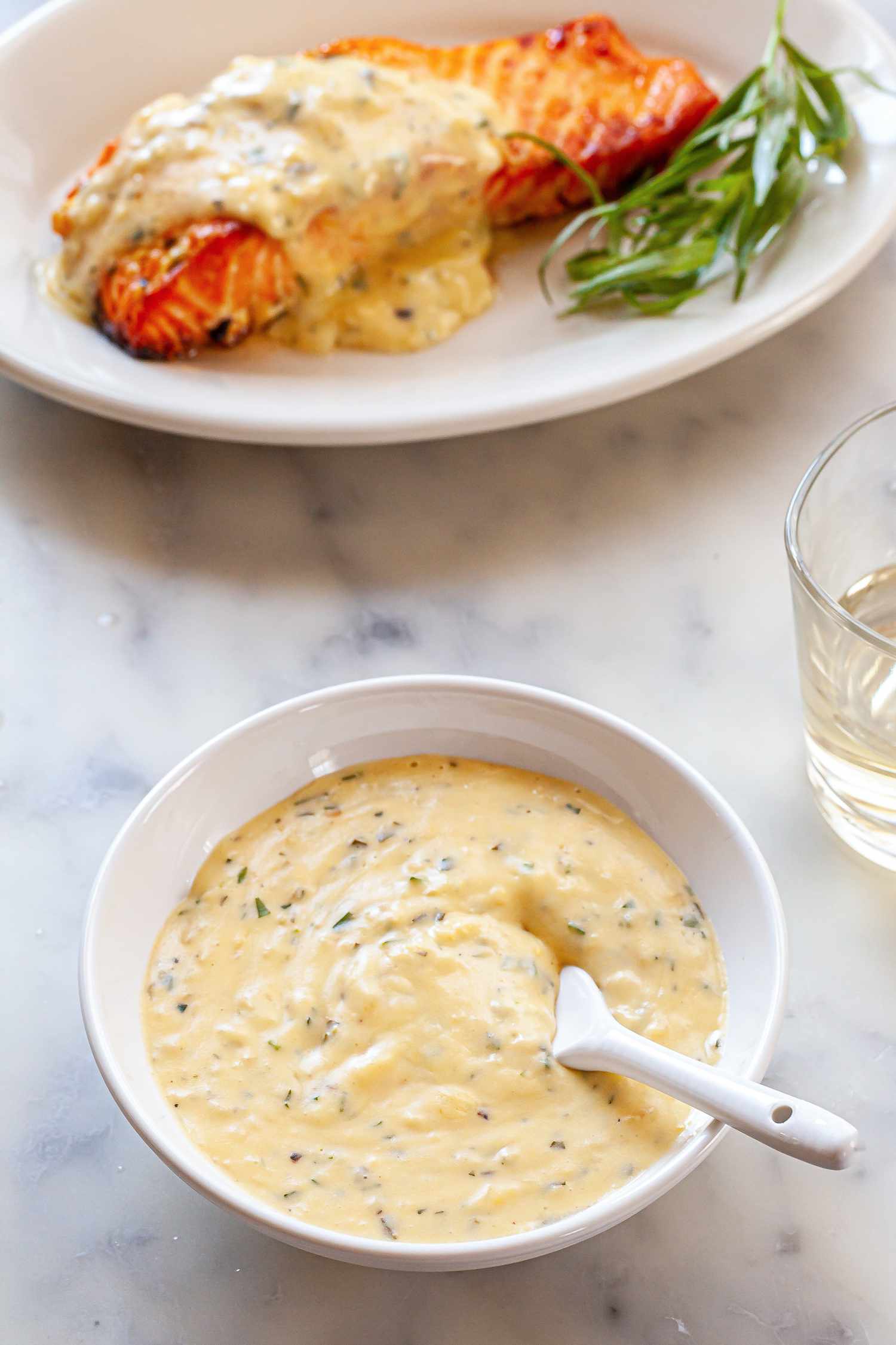 Classic mother sauce: béarnaise in a bowl with a plate of salmon and sauce set behind the bowl.